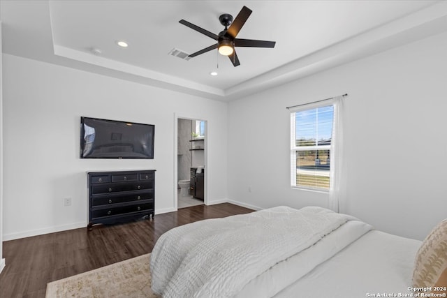 bedroom with a tray ceiling, connected bathroom, ceiling fan, and dark wood-type flooring