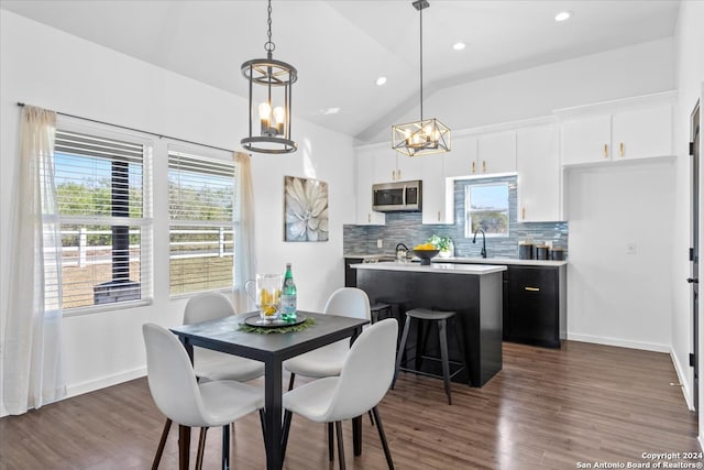 dining space with dark hardwood / wood-style floors, lofted ceiling, sink, and an inviting chandelier