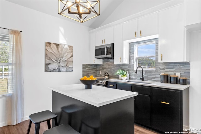 kitchen with sink, light wood-type flooring, decorative light fixtures, white cabinetry, and a breakfast bar area