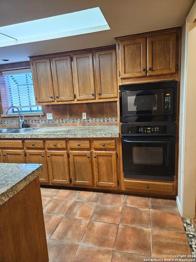 kitchen featuring a skylight, sink, light tile patterned floors, and black appliances