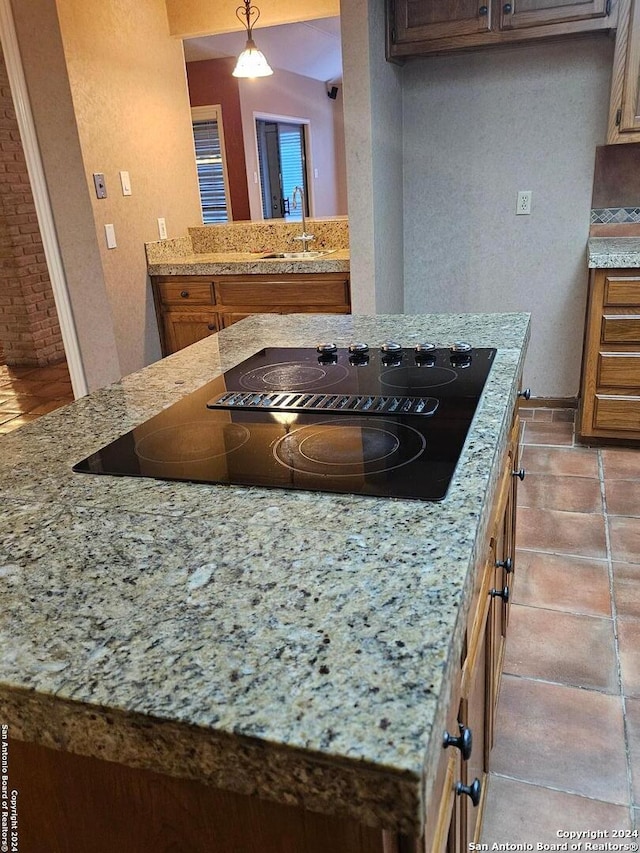 kitchen featuring light stone countertops, sink, pendant lighting, black electric cooktop, and light tile patterned floors