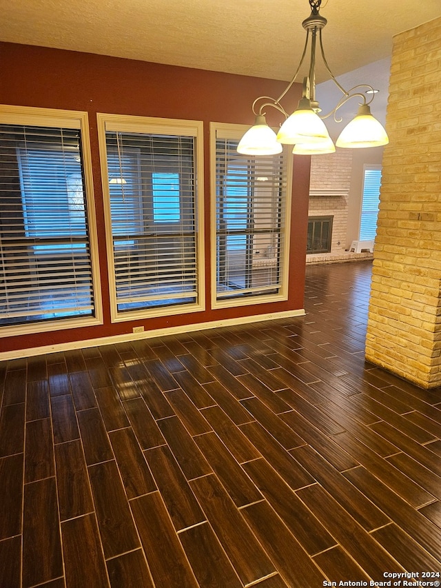 unfurnished dining area with a textured ceiling, a notable chandelier, dark hardwood / wood-style floors, and a brick fireplace