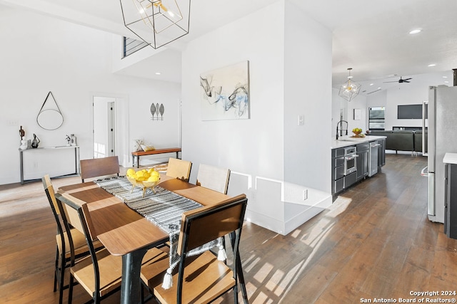 dining area featuring ceiling fan with notable chandelier, dark hardwood / wood-style floors, sink, and vaulted ceiling