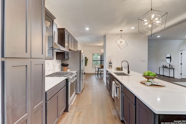 kitchen featuring sink, wall chimney exhaust hood, light hardwood / wood-style flooring, pendant lighting, and appliances with stainless steel finishes