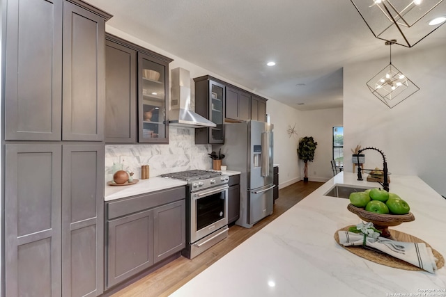 kitchen with sink, light hardwood / wood-style flooring, wall chimney exhaust hood, decorative light fixtures, and stainless steel appliances