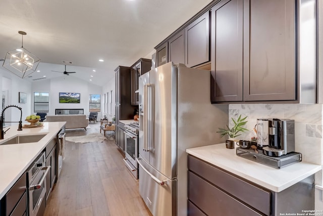 kitchen featuring pendant lighting, sink, vaulted ceiling, premium appliances, and light hardwood / wood-style floors