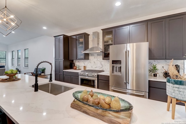 kitchen with decorative backsplash, wall chimney exhaust hood, stainless steel appliances, sink, and hanging light fixtures