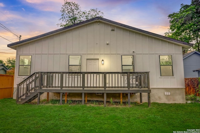 back house at dusk featuring a wooden deck and a lawn