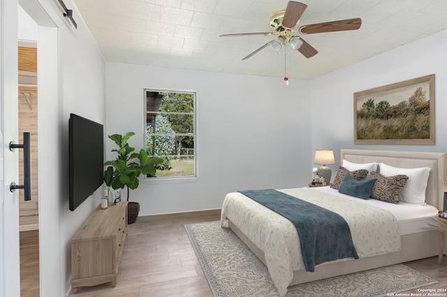 bedroom featuring a barn door, ceiling fan, and wood-type flooring