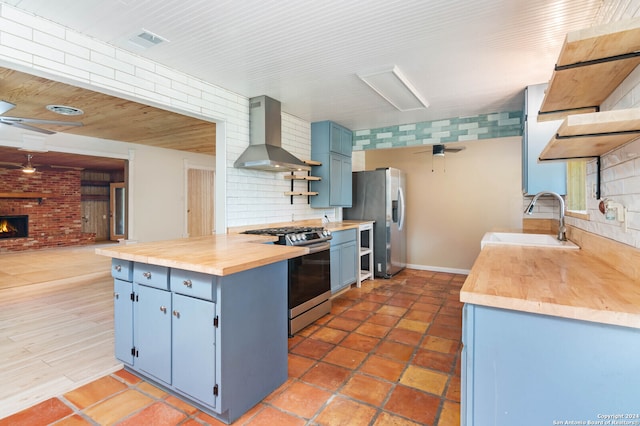 kitchen featuring wood counters, appliances with stainless steel finishes, wall chimney exhaust hood, sink, and a fireplace