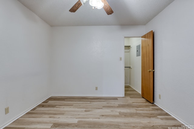 empty room featuring a textured ceiling, light wood-type flooring, electric panel, and ceiling fan