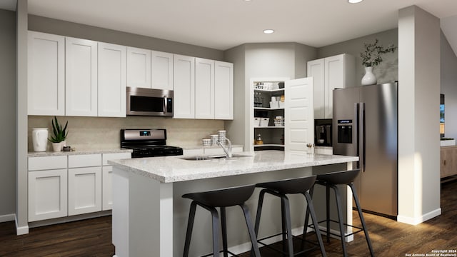 kitchen featuring dark wood-type flooring, stainless steel appliances, white cabinetry, and a center island with sink