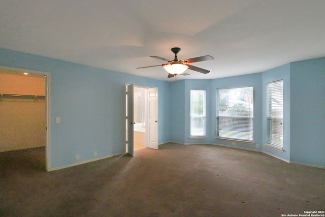 interior space with a spacious closet, a closet, ceiling fan, and dark carpet