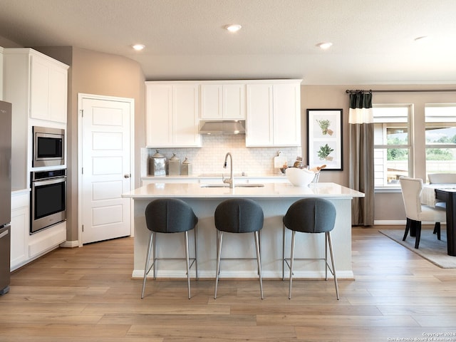 kitchen featuring stainless steel appliances, a kitchen island with sink, sink, and white cabinets