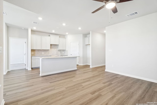 kitchen with backsplash, ceiling fan, light hardwood / wood-style floors, white cabinetry, and an island with sink