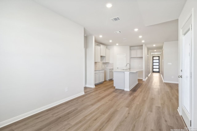 kitchen with sink, light hardwood / wood-style flooring, decorative backsplash, a center island with sink, and white cabinets