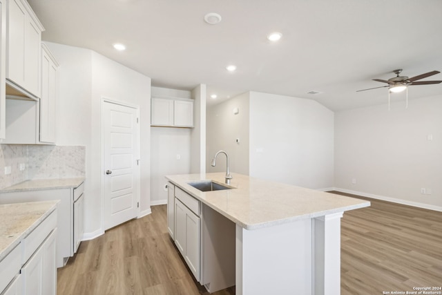 kitchen featuring a center island with sink, white cabinetry, light hardwood / wood-style floors, and light stone counters