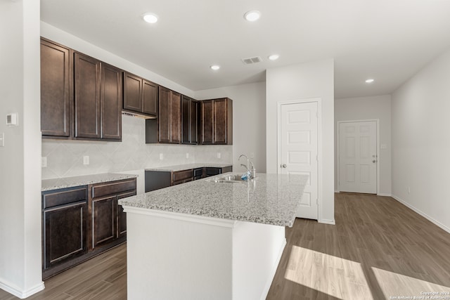 kitchen with sink, light hardwood / wood-style floors, light stone counters, and an island with sink