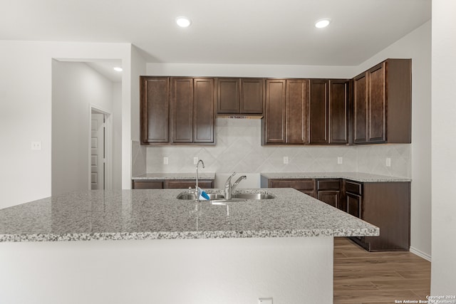 kitchen with hardwood / wood-style floors, light stone counters, dark brown cabinetry, and sink