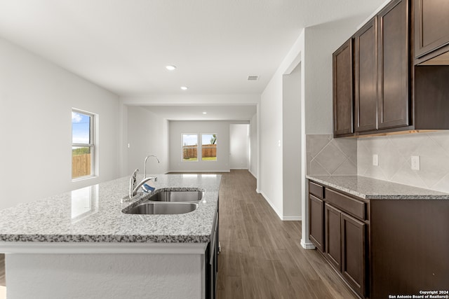 kitchen with wood-type flooring, sink, decorative backsplash, light stone counters, and dark brown cabinetry