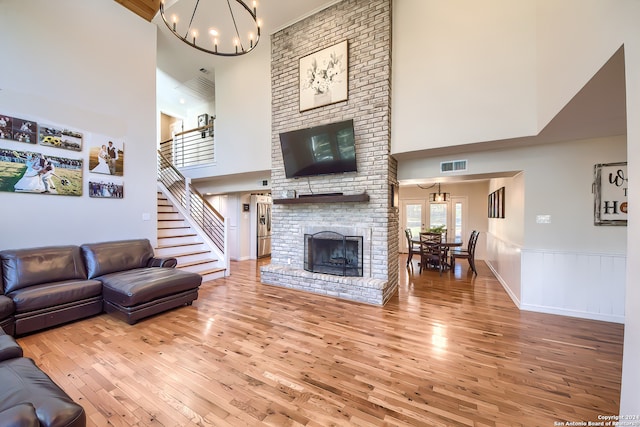 living room featuring hardwood / wood-style flooring, a towering ceiling, a brick fireplace, and an inviting chandelier