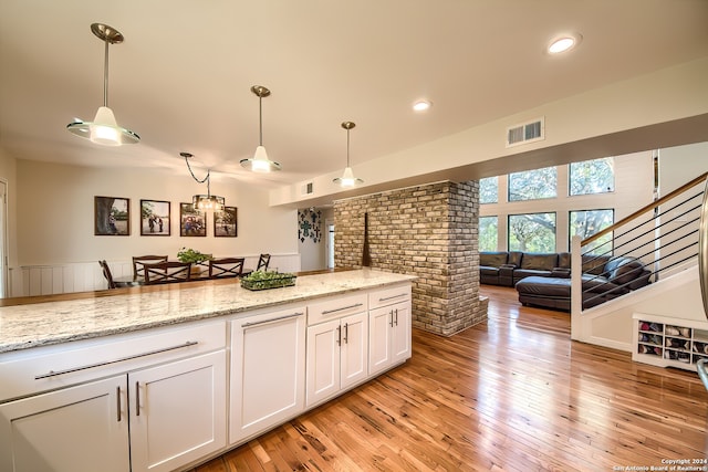 kitchen with light wood-type flooring, decorative light fixtures, white cabinetry, and light stone counters