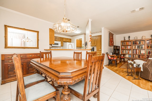 dining space with sink, light hardwood / wood-style floors, crown molding, and a notable chandelier