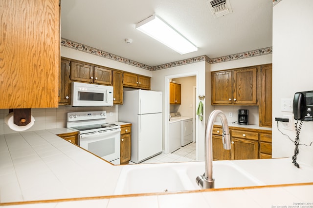 kitchen featuring washing machine and clothes dryer, sink, tile countertops, kitchen peninsula, and white appliances