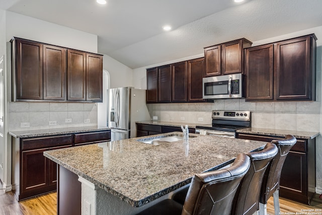 kitchen with a kitchen breakfast bar, an island with sink, lofted ceiling, appliances with stainless steel finishes, and light wood-type flooring