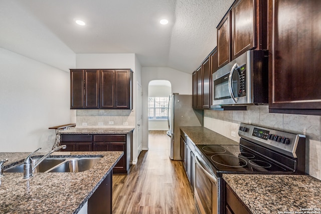 kitchen featuring sink, dark stone countertops, light hardwood / wood-style floors, vaulted ceiling, and appliances with stainless steel finishes