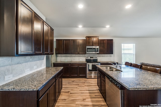 kitchen with sink, tasteful backsplash, dark brown cabinets, appliances with stainless steel finishes, and light wood-type flooring