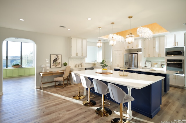 kitchen with light wood-type flooring, stainless steel appliances, a kitchen island, pendant lighting, and white cabinetry