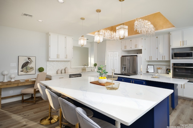 kitchen with light hardwood / wood-style flooring, a kitchen island, white cabinetry, stainless steel appliances, and a chandelier