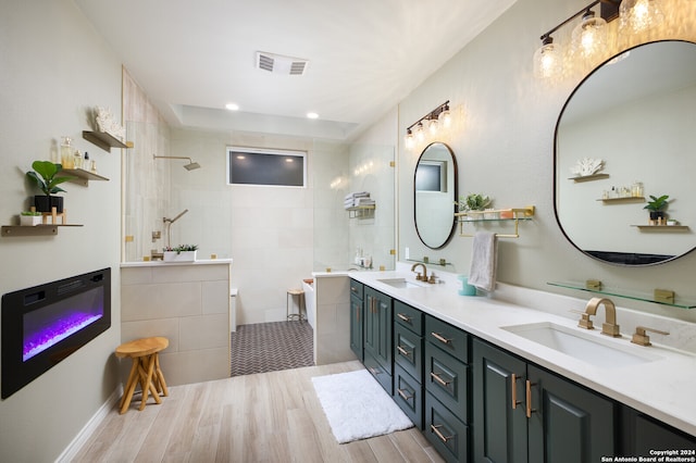 bathroom with hardwood / wood-style floors, vanity, a tile shower, and tile walls