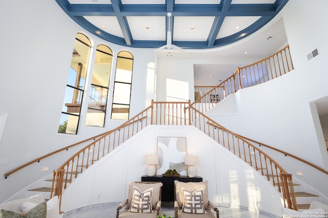 stairway featuring beam ceiling, a towering ceiling, and coffered ceiling