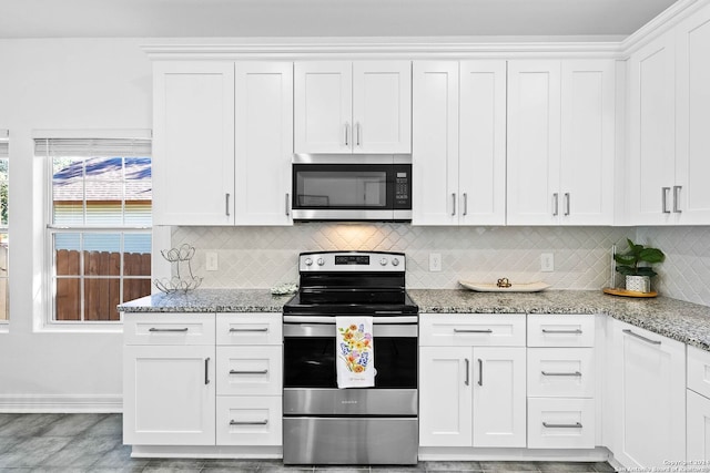 kitchen featuring white cabinets, appliances with stainless steel finishes, decorative backsplash, and light stone countertops