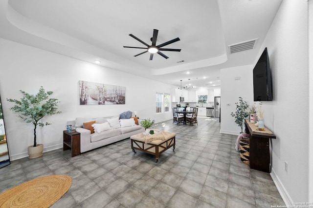 living room featuring ceiling fan with notable chandelier and a raised ceiling