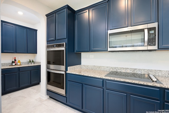 kitchen featuring light tile patterned flooring, light stone counters, blue cabinetry, and appliances with stainless steel finishes