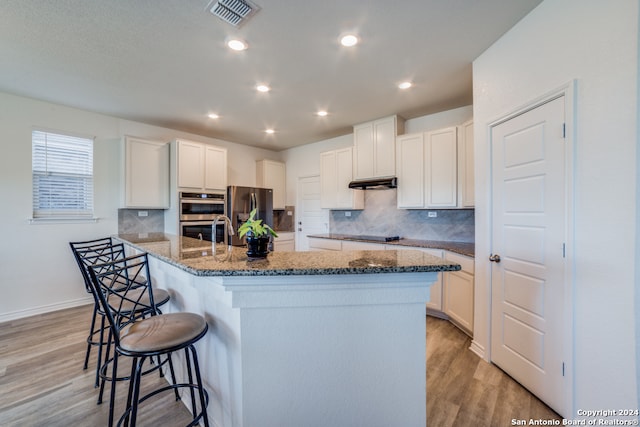 kitchen featuring a kitchen island with sink, stainless steel appliances, dark stone counters, and white cabinets