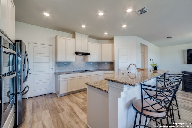 kitchen with a kitchen island with sink, white cabinets, and light stone counters