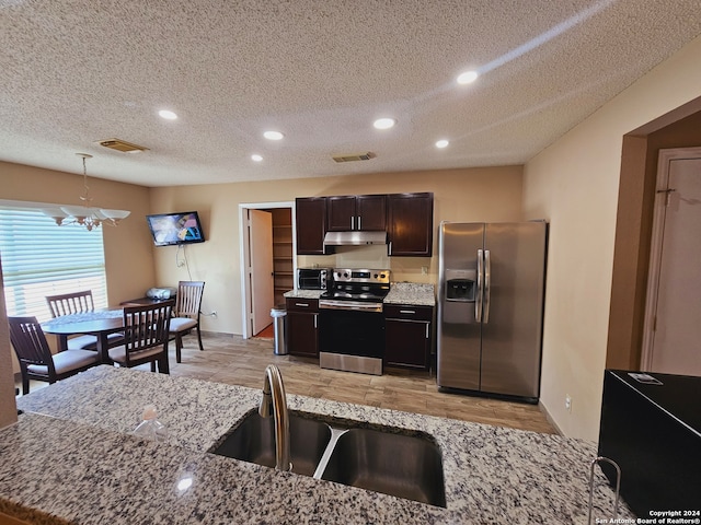 kitchen with light stone counters, stainless steel appliances, sink, decorative light fixtures, and light hardwood / wood-style flooring