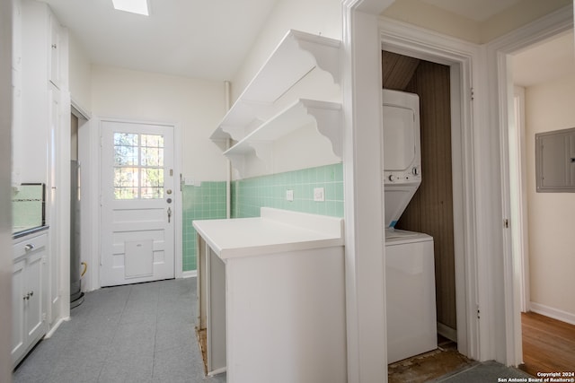 washroom featuring stacked washer / dryer, electric panel, light tile patterned flooring, and tile walls