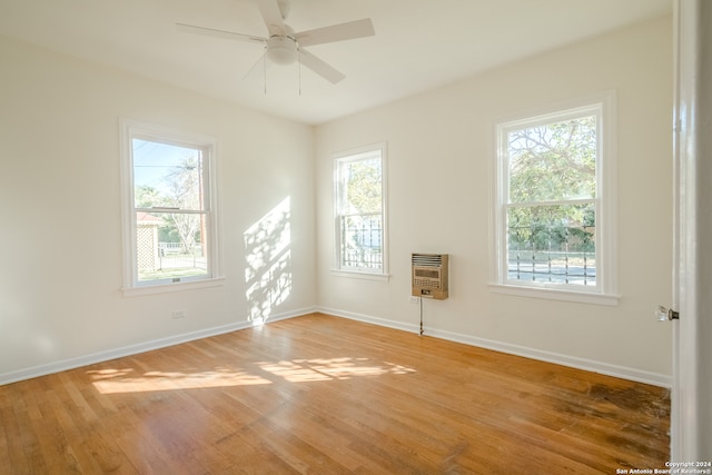 unfurnished room with ceiling fan, wood-type flooring, a wealth of natural light, and heating unit