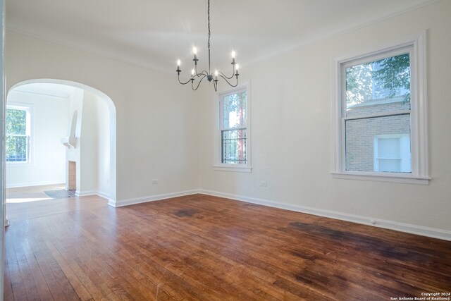 empty room with crown molding, a chandelier, hardwood / wood-style floors, and a healthy amount of sunlight