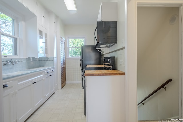 kitchen with wooden counters, black range with electric cooktop, white cabinetry, and a healthy amount of sunlight