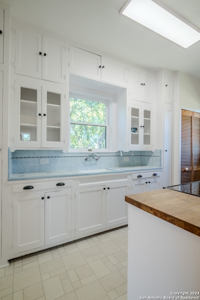 kitchen with butcher block countertops, white cabinets, sink, and tasteful backsplash