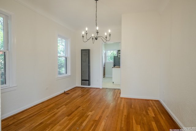 unfurnished dining area with wood-type flooring, a wealth of natural light, and an inviting chandelier