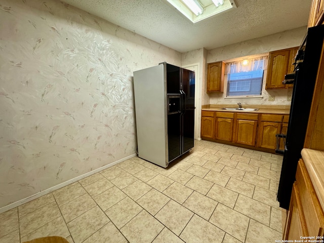 kitchen with sink, a textured ceiling, black refrigerator with ice dispenser, and a skylight