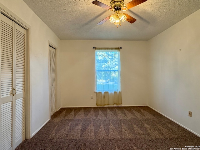 unfurnished bedroom featuring dark colored carpet, a textured ceiling, two closets, and ceiling fan