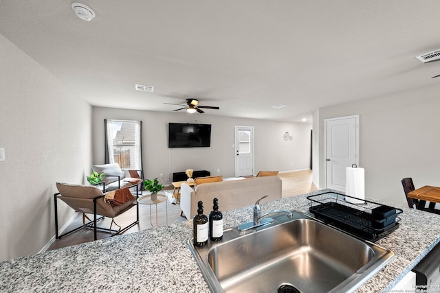 kitchen featuring light stone countertops, a breakfast bar, ceiling fan, sink, and dark hardwood / wood-style floors